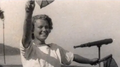 Friends of Coastal Forces A black and white photo of a young, smiling Eve Branson in naval uniform signalling with flags.