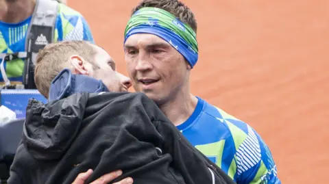 PA Media Sinfield carrying Burrow over the finishing line at the Rob Burrow Leeds Marathon