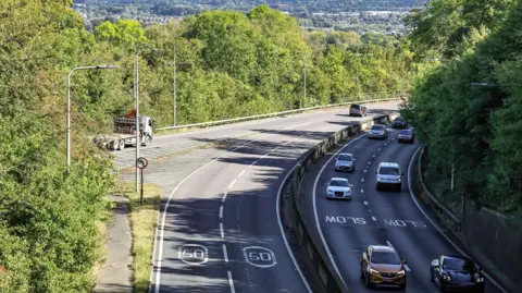 The image shows an aerial shot of the A3, where cars can be seen driving and a lorry is merging onto the motorway
