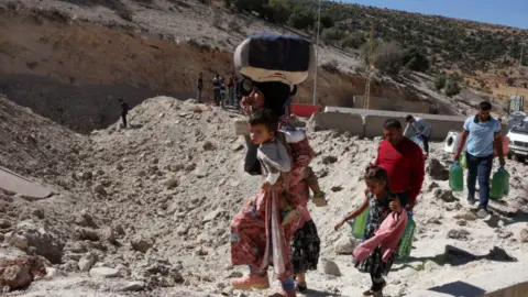 Reuters A family with two children walk on foot - the mother bearing her youngest and several bags - past the cratered road at the Masnaa crossing into Syria on 4 October