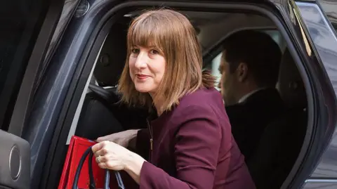 Chancellor Rachel Reeves getting out of a cab outside Downing Street in May, wearing a maroon suit and carrying a handbag and red folder