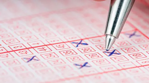 Getty Images A silver pen hovers over a lottery ticket - some of the numbers already have blue ink Xs through them
