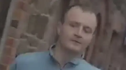 PSNI A still image taken from a video showing a man with short brown hair and wearing a blue quarter-zip.