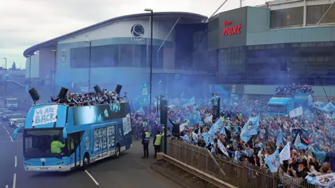PA Media The bus leaving the CBS Arena with a large crowd behind fencing on the right