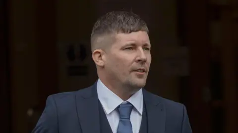 A man wearing a navy suit, blue shirt and blue tie.