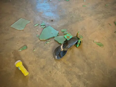 Gift Ufoma / BBC A sandal next to a torch and broken pieces of glass in a dormitory with beds at St Mary's boarding school in Papiri village in Niger state.