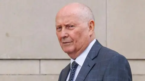 PA Media Frank Cushnahan, a man with short grey hair, wearing a grey suit, a white tie and dark tie with white dots.