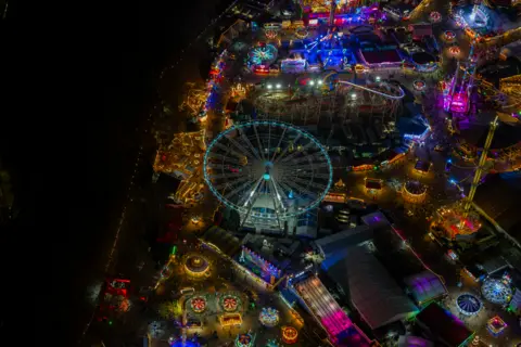 Jason Hawkes Aerial photograph taken at night showing Ferris wheels, roller coaster and other rides lit up in different colours in Winter Wonderland