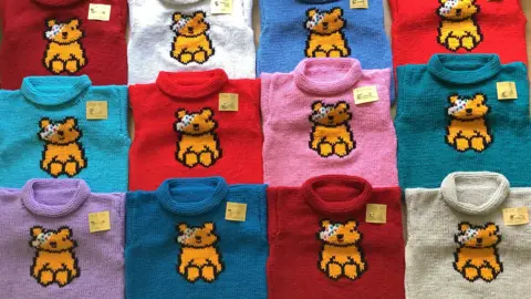 Different coloured knitted jumpers with Pudsey on them lined up