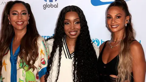 Getty Images Left to right Su-Elise Nash, Sabrina Washington and Alesha Dixon pose on the red carpet at Capital's Summertime Ball. They're all smiling for the camera and have a white board behind them has logos on it like Global and Capital Summertime Ball.