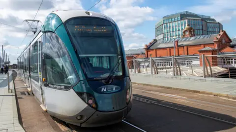 A green and silver tram at a stop.