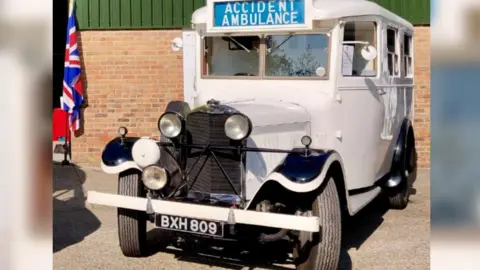 An old white ambulance with with "accident ambulance written on a blue sign upon it