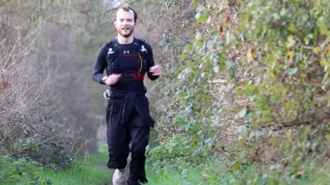 Jack runs towards the camera along a countryside footpath which has hedges on either side. 