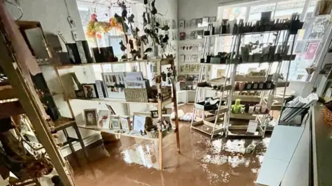 Jenny Chuter The image shows Jenny's shop with shelves full of pictures, candles and cards, but the floor is completely covered in water. 