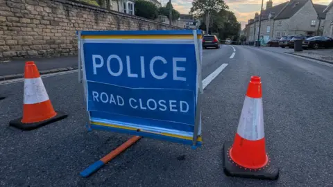A blue police road closed sign sits between two orange cones on Oxford Street in Woodstock.