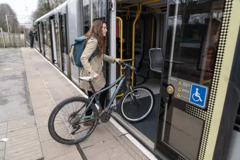 Transport for Greater Manchester A woman getting on a tram with a bicycle 