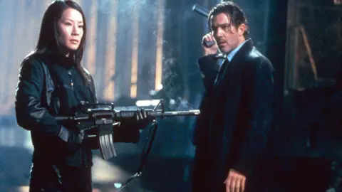 Sipa/Shutterstock Lucy Liu y Antonio Banderas de pie con todas las armas negras y sosteniendo armas en una escena de Ballistic: Ecks vs Sever