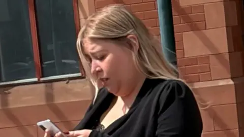 Ilona Robinson. She is wearing black and looking at a mobile phone
