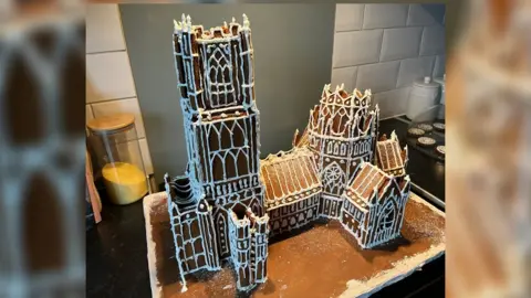 John Devine Ely Cathedral in Gingerbread, made by Owen Angier, the model is nearly 60cm (2ft) long and just over 30cm (1ft) high. It has white icing around the doors and windows, and he melted boiled sweets to make edible stained glass windows.