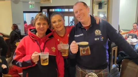 Francesca Murphy Francesca stands successful  the mediate  of her mum and dada  successful  a pub. They are each  smiling and looking blessed  and are holding pints of beer.