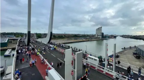 An aerial view of Gull Wing Bridge in Lowestoft. There are people walking across the bridge, with a view to the right of Lake Lothing.