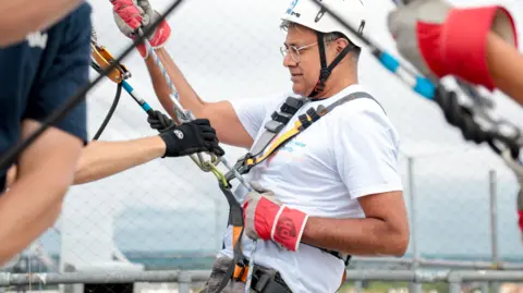Fred Mendonca wearing a helmet and attached to ropes as he leans back to abseil.