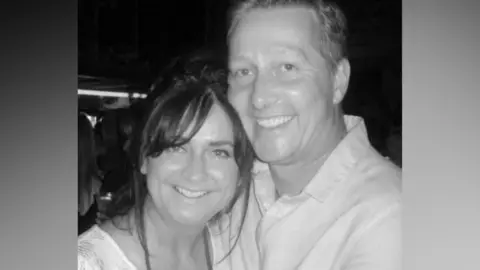 A black and white photo of a man and woman. They are smiling and hugging each other.