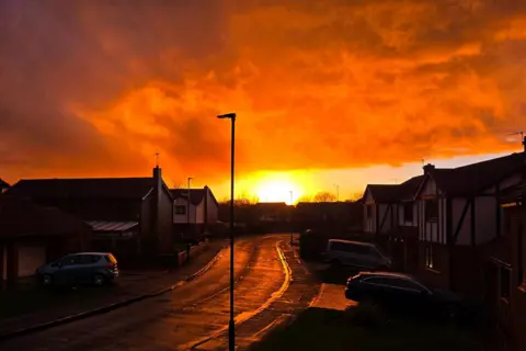 BBC Weather Watchers / Dave-by-the-sea A residential street is illuminated as the sun sets. The clouds are a bright orange colour.