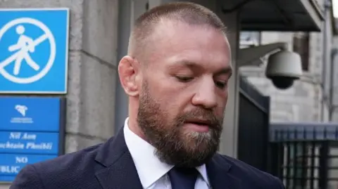 Brian Lawless/PA Wire Conor McGregor outside the High Court in Dublin. He has a beard, shaved hair and wears a navy blue suit and white shirt.