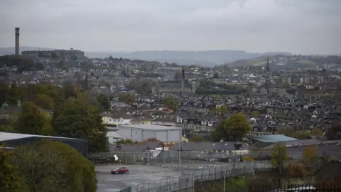 The Bradford skyline, viewed on a cloudy day. Rows of housing, trees and industrial buildings can be seen. 
