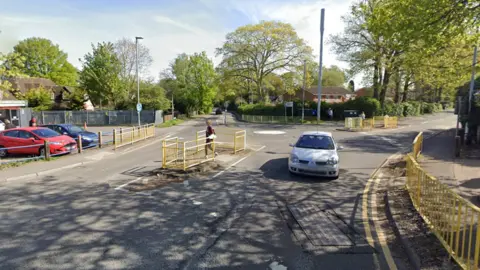 Google shows screenshots from Google Street View what the area looked like. The middle has a mini roundabout with a white painted island. There is no crossing on the exit, just the gaps in the yellow pavement railing suggest that people can cross there.