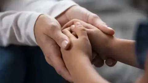 Getty Images A close up of an adult's hands holding a child's hands. 