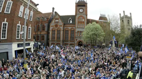 Reading FC A large group of Reading supporters stood in front of the grey and orange town hall.
