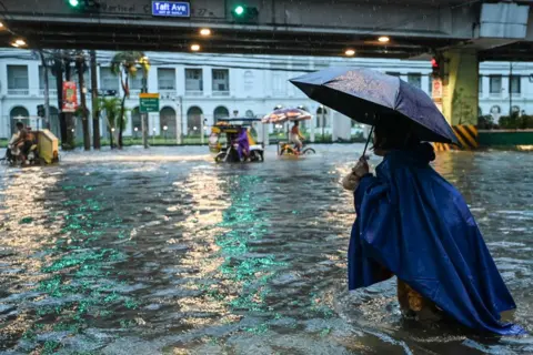 Jam Sta Rosa/AFP People walk along a flooded street in Manila on July 24, 2024 amid heavy rains brought by Typhoon Gaemi. 