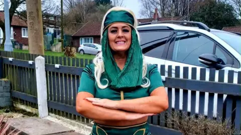 Lisa Hughes Woman stands in a green pharoh outfit dressed as Egyptian Pharoh Tutankhamun.