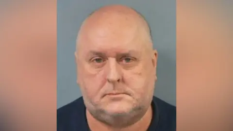 A bald man with some stubble poses for a custody image.