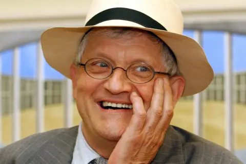 PA Media David Hockney smiling in glasses and a hat in 2004