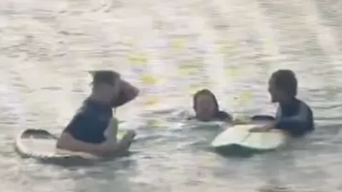 Two surfers with boards and a young woman swimming between them.