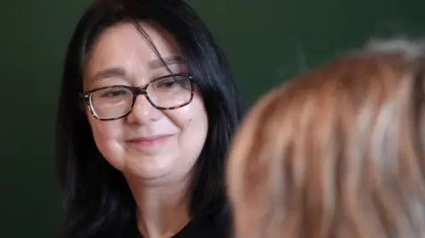 Catherine Flutsch has shoulder-length black hair and is wearing tortoiseshell glasses.