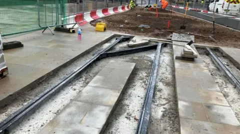 Bridge Street Tramlines set into a gap between newly laid paving slabs, with workmen wearing high vis jackets in the background