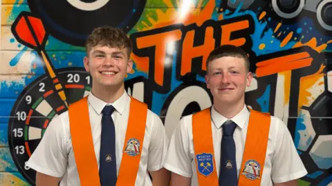 Two young teenagers smiling at the camera wearing white shirts and orange collarettes