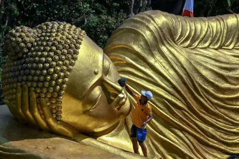JUNI KRISWANTO/AFP A worker cleans a Buddha statue at the Maha Vihara Mojopahit temple in Mojokerto on 15 May 2024