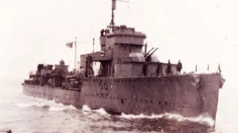 Supplied An old black and white image of a large warship in the water with the number L29 on the side.