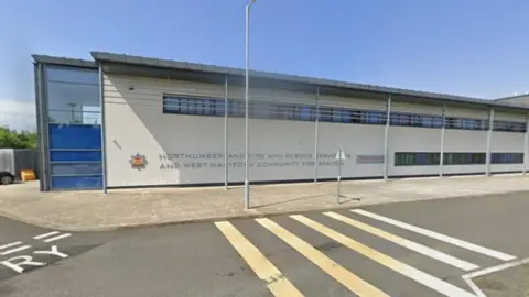 Northumberland Fire and Rescue HQ at West Hartford. It is a low industrial building with narrow windows on two floors. The name of the service and its logo appear on a large section of light coloured wall with a glazed section to the left.
