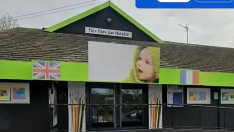 Picture of the front of Tiny Toes nursery from outside. There is a sign and picture of a baby above the front doors. 