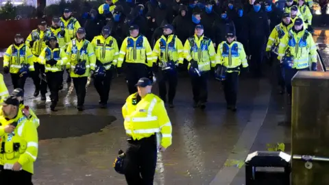 A line of police in yellow high-vis walk in front of Rangers fans in Manchester, ahead of their team's UEFA Europa League League Stage fixture against Manchester United.