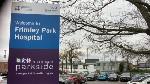 BBC General view of hospital with car park and signage in the foreground.