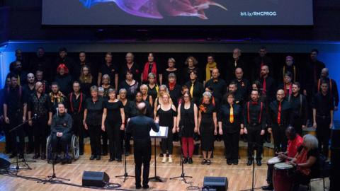 Part of the LGBTQ+ community singing with conductor in front at previous choir festival