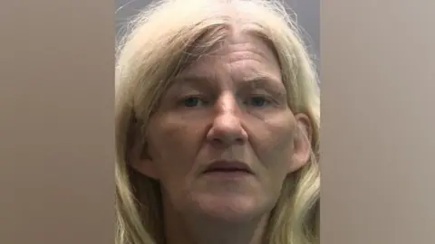 Jacqueline Mounsey is a 53-year-old woman with straight thick blond shoulder-length hair which she has tucked behind her ears. You can only see her head, she is not smiling. 