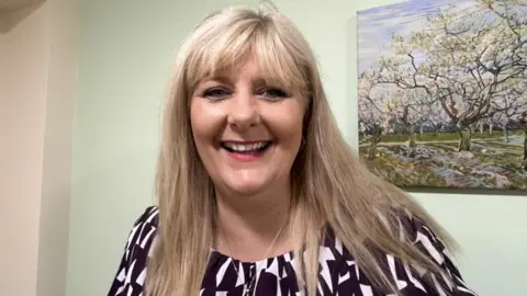 A woman with blond hair and a black and white top smiling